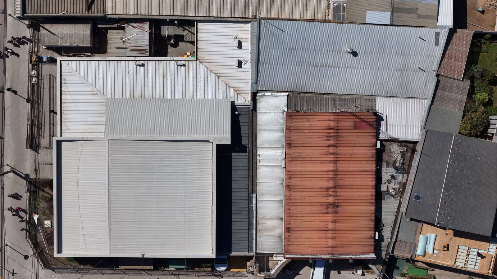 Top-down view of multiple industrial warehouse roofs with varying textures and colors, some with skylights or vents.