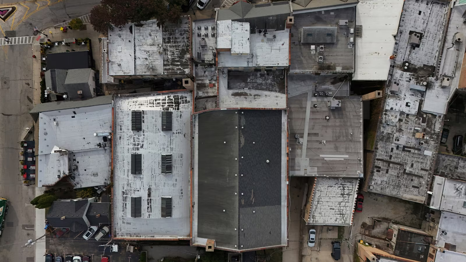 Top-down aerial view of various rooftops in an urban area, showing different materials and conditions.